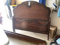 Wooden vintage bed frame in a garage room, showing the entire bed frame including headboard and footboard laid out flat.