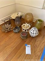 Full set of glass and metal candle holders arranged on the floor showing colors and shapes.