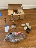 Photo showing all items: damaged three-arm sterling silver candlestick, wrapped double-arm candlestick, mini silver cup with four saucers, crystal glass with silver rim on cardboard box.