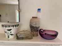 Photo showing all four items: ceramic plant pot, ceramic vase, and two glass ashtrays on a white surface.