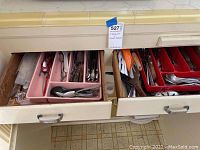 Two kitchen drawers open, showing assorted flatware in pink and red plastic trays.