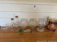 Photo showing all glass items placed on a wooden surface including three balloon-shaped holders, small jars, bottle, stopper, and marbles