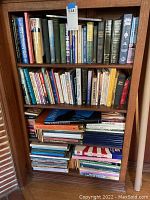 Full view of wooden bookshelf filled with approximately 50 assorted hardbound books, arranged on three shelves and two bottom stacks. Titles visible relate to nonfiction, spirituality, and gardening.