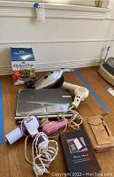 Photo showing a Gateway laptop, Dirt Devil hand vacuum, a boxed Kitchen Crop sprouter, three hair dryers, a brown leather personal organizer, and business calculator on hardwood floor.