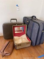 Photo showing all four items: large gray luggage, brown suitcase, brown leather pouch, and open vanity case with red interior and dental molds