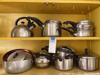 Wide view of pots, pans, and kettle arranged on shelves showing variety and condition.