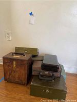 Group photo of six vintage boxes including a wooden precision sharpening box and metal lock boxes in green and brown finishes on wooden floor.