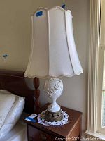 Full view of vintage table lamp with white fabric shade, ceramic body, and metal base on a nightstand.