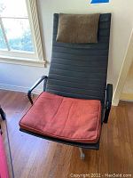 Front view of chair showing black ribbed upholstery, red seat cushion and brown pillow