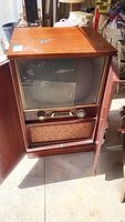 Front view of vintage tube television inside wooden cabinet with doors open, showing screen, knobs, and speaker area.