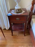 Full view of vintage wood nightstand with lamp on top, showing overall condition and size.
