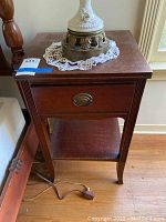 Front view of the vintage wooden nightstand showing single drawer with oval brass pull and lower shelf. Top surface has scratches.