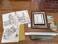 Photo of lot showing four architectural black and white prints, framed artwork, two small wood panel paintings, and two rolled canvases on wooden floor.