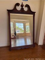 Wall mirror with an ornately carved dark wood frame, rectangular shape, top central finial, visible scratches on mirror surface.