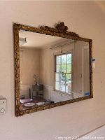 Full view of large rectangular wall mirror with ornate carved gold frame mounted on wall.