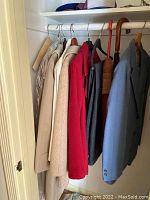 Photo of various women's coats and jackets hanging on a rack with two umbrellas visible