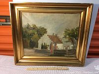 Frontal view of the framed oil painting showing a church and trees in landscape with ruler for scale reference.