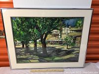 Framed watercolor showing a tree-lined street with buildings and signage