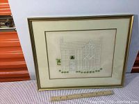 Full view of the framed Irish cross stitch artwork titled 'St. Pattys Inn' showing the gold frame and double matting on a white background with ruler for size reference.