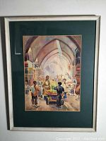 Framed watercolor painting showing a market scene inside arched corridor with multiple figures. Original frame and green mat visible.