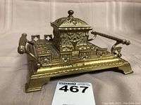 Front angled view of ornate brass inkwell showing decorative base and hinged lid