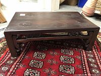 Front view of low rectangular wooden tea table showing carved fretwork apron and dark brown top