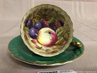 Front view of teacup set in saucer showing interior fruit painting and green exterior