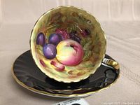 Teacup and saucer showing interior fruit motif and scalloped edge
