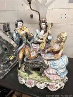 Full front view of porcelain figural lamp showing three musicians and harp arm for shade