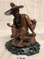 Front view of full sculpture showing seated figure, pipe, basket and wooden base