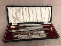 Open presentation case showing four stag-handled tools in red velvet and white satin lining