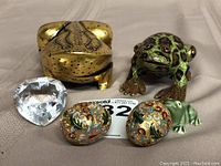 Overview of all items: cloisonne frog and eggs, lacquered frog box, crystal paperweight, zinc miniature frog