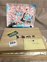 Tray displayed on stand in front of wooden presentation box with Japanese writing and document inside box.