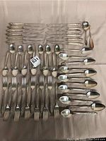 Twelve dinner knives, forks, tablespoons, teaspoons and three serving pieces arranged on tablecloth