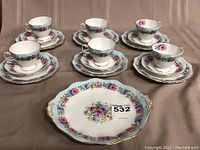 Six tea cups arranged on six saucers and luncheon plates with sandwich platter in front