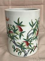 Front view of white cylindrical porcelain vase showing hand-painted branches with leaves and pinkish-red fruit, and orange decorative marking.