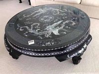Front view of round black lacquer low tea table with glass top and mother of pearl inlay