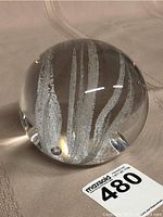 Clear four inch glass spherical paperweight showing internal abstract silver-white formations with reflections on fabric surface