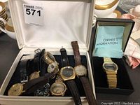 Eight analog watches arranged in white lined case with one boxed digital watch visible at right