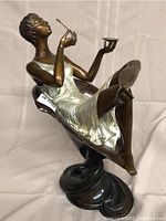 Front three-quarter view showing figure reclining on swirling base, holding bowl and tool