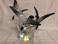 Front view of sculpture showing two birds diving and one ascending from clear glass base