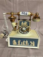 Front view of telephone showing cream resin base, classical relief panels, rotary dial and gold-tone handset cradle