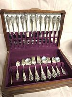 Open wooden presentation case showing two tiers of flatware on purple velvet lining