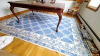 Blue and cream area rug with chain-link and floral patterns under a wooden table in a room with hardwood floors and natural light from windows.