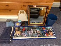 Full lot items showing from left to right: three folded towels, two lamp shades (one large fabric and one smaller blue), table lamp base, small plate with soap, blue wastebasket, Audubon Zoo poster, framed mirror leaning against the wall
