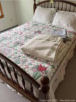 Queen bed with floral patchwork quilt, matching pillowcases, bedskirt, and beige textured blanket folded on top.