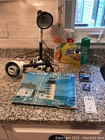 Photo showing the New England Coast book, cleaning supplies including Glade, Lysol, Goof Off, Spray Starch, two batteries, and two task lamps on a counter.