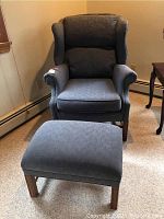 Blue upholstered wing back chair and matching ottoman in room setting, showing full view from an angle