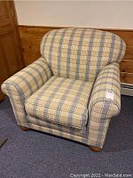 Front and side view of the upholstered armchair showing plaid fabric upholstery, rounded backrest, padded arms, and wooden legs.