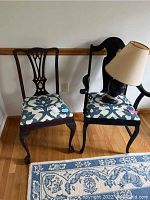 Two dark painted wood chairs with blue and white patterned upholstered seats placed side by side, one with a beige lamp on it.